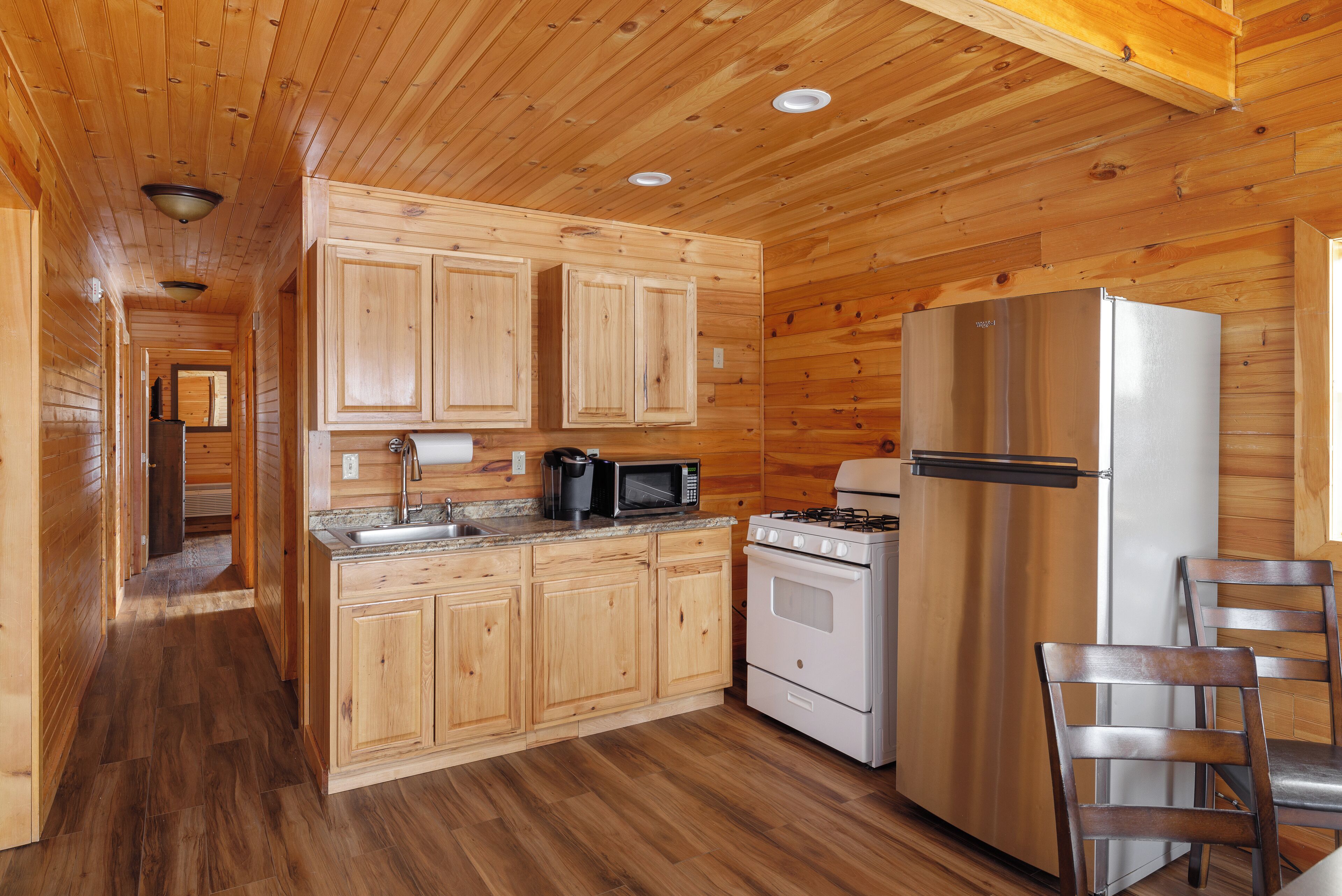 A wooden cabin kitchen with a stove, microwave, and refrigerator.