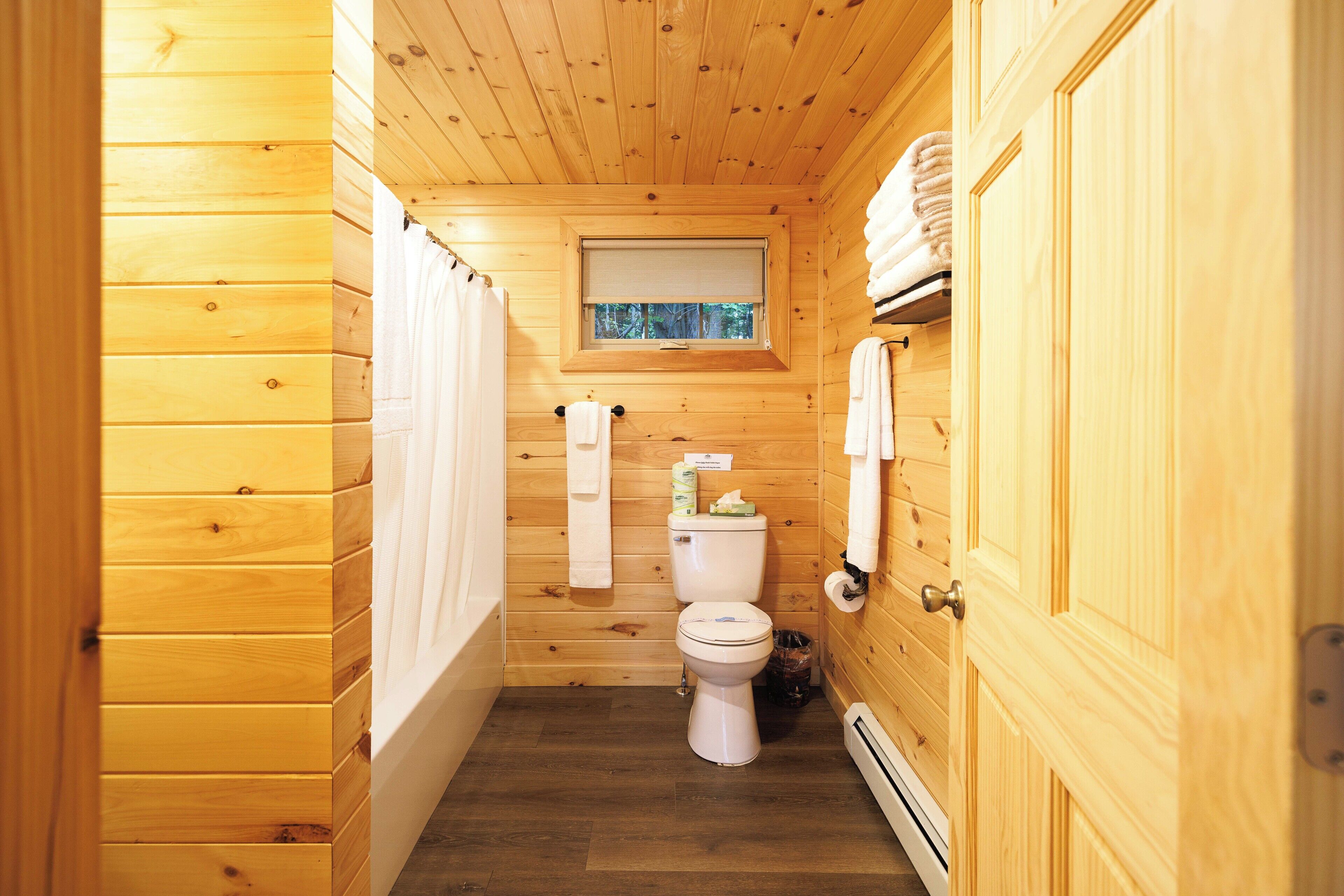 Een houten badkamer in een vakantiehuisje, met toilet, raam en handdoekhouder.