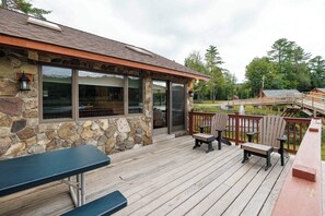 A stone building with large windows and a wooden deck with benches and a table.