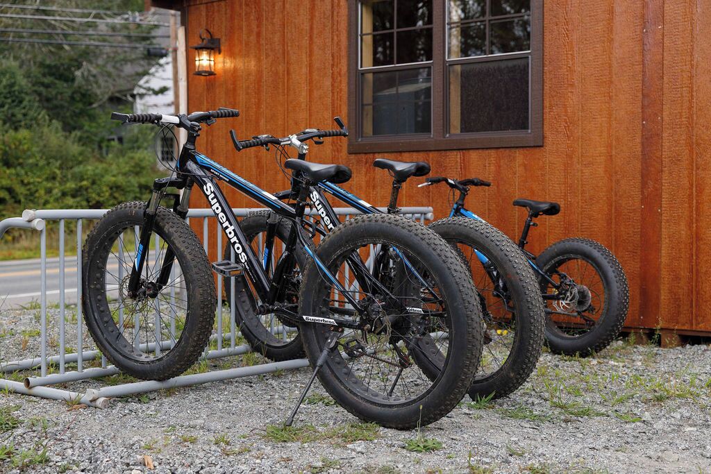 Three bicycles parked in front of a wooden building with a window and a light fixture.