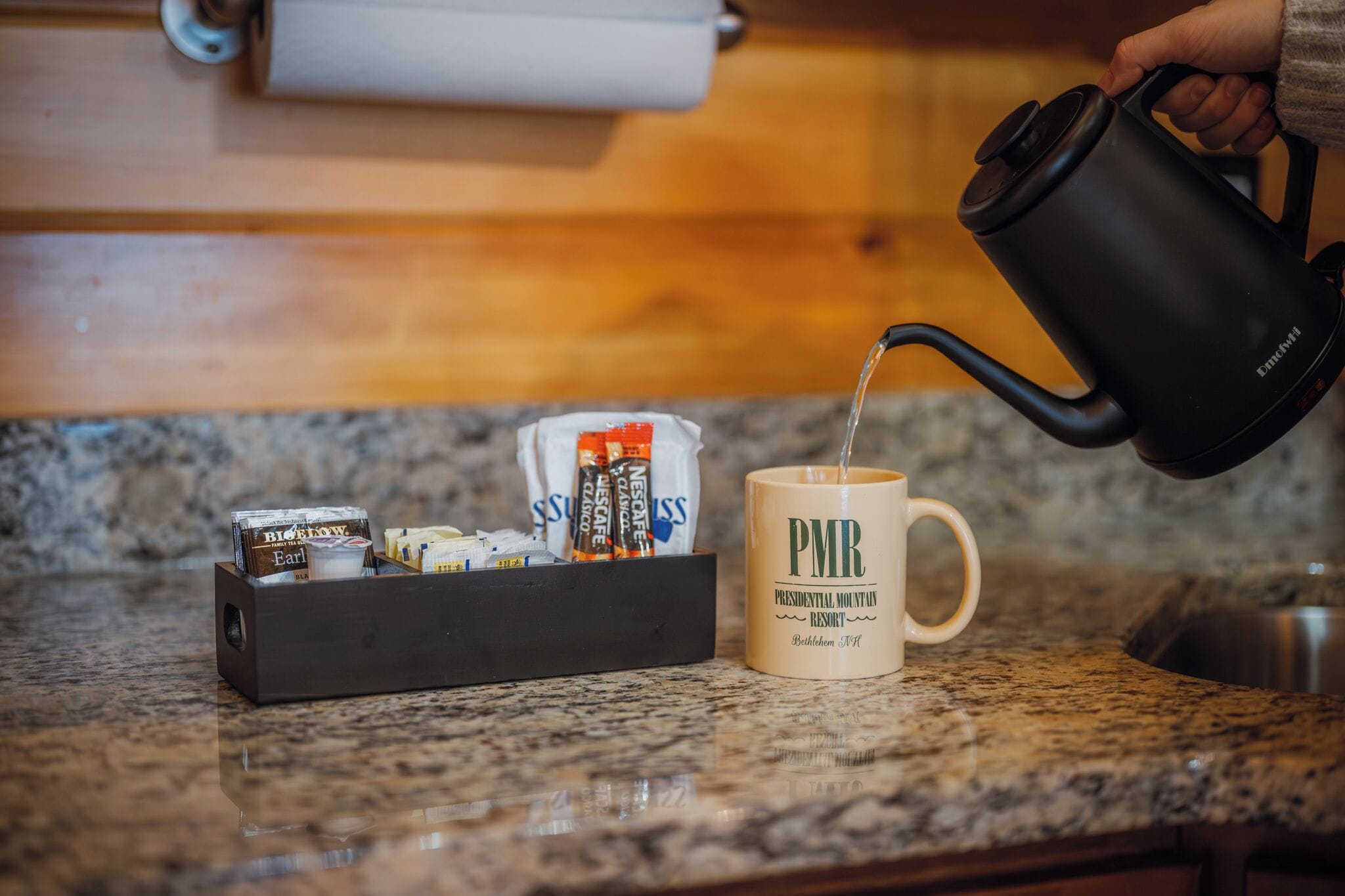 A coffee maker pouring water into a mug labeled "PMR Presidential Mountun Resort."
