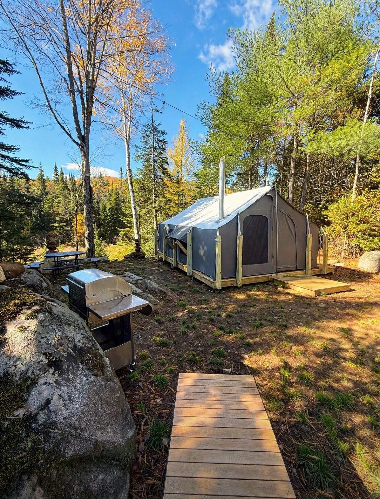 A camping site with a tent, a grill, and a wooden deck.