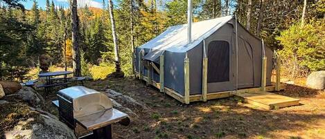 A camping site with a tent, a grill, and a wooden deck.