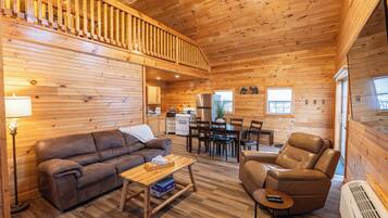 Ein Ferienhaus-Innenraum mit einer Couch, einem Sessel, einem Esstisch, einer Küchenzeile und einer Treppe.