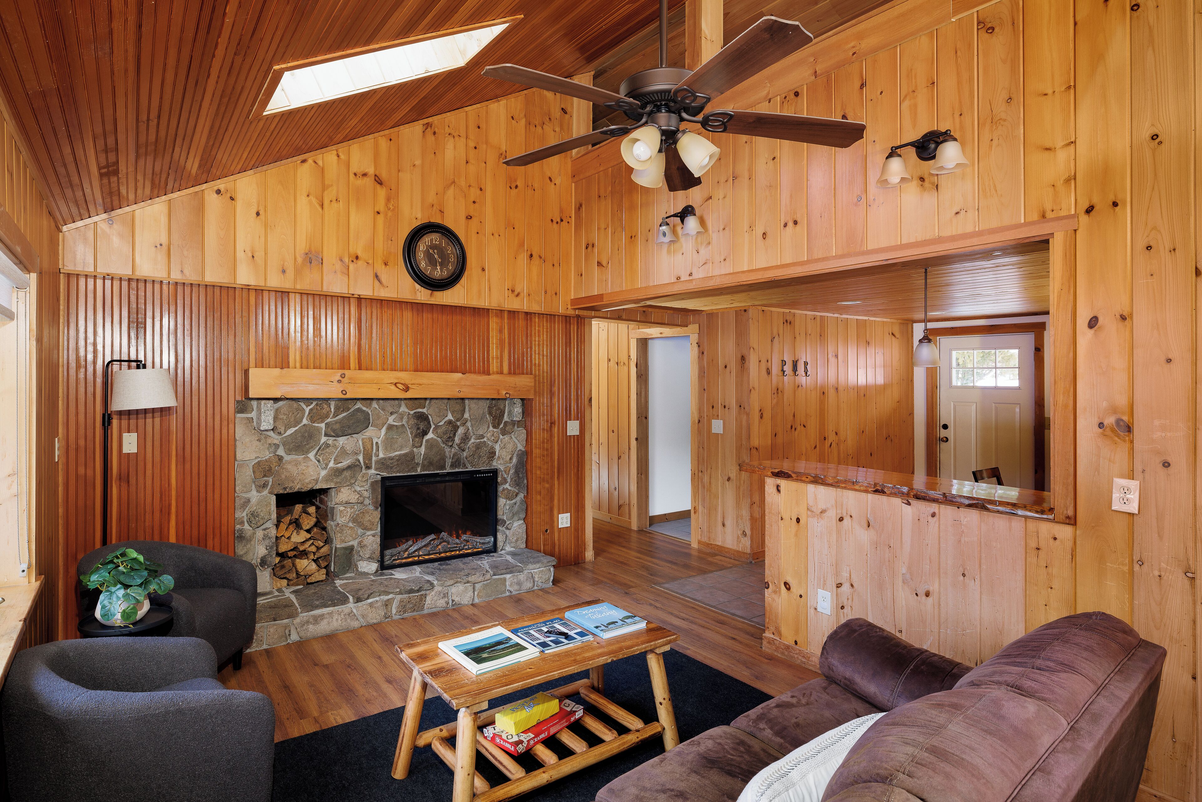 A wooden interior with a stone fireplace, a ceiling fan, and a couch.