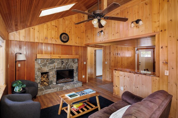 A wooden interior with a stone fireplace, a ceiling fan, and a couch.