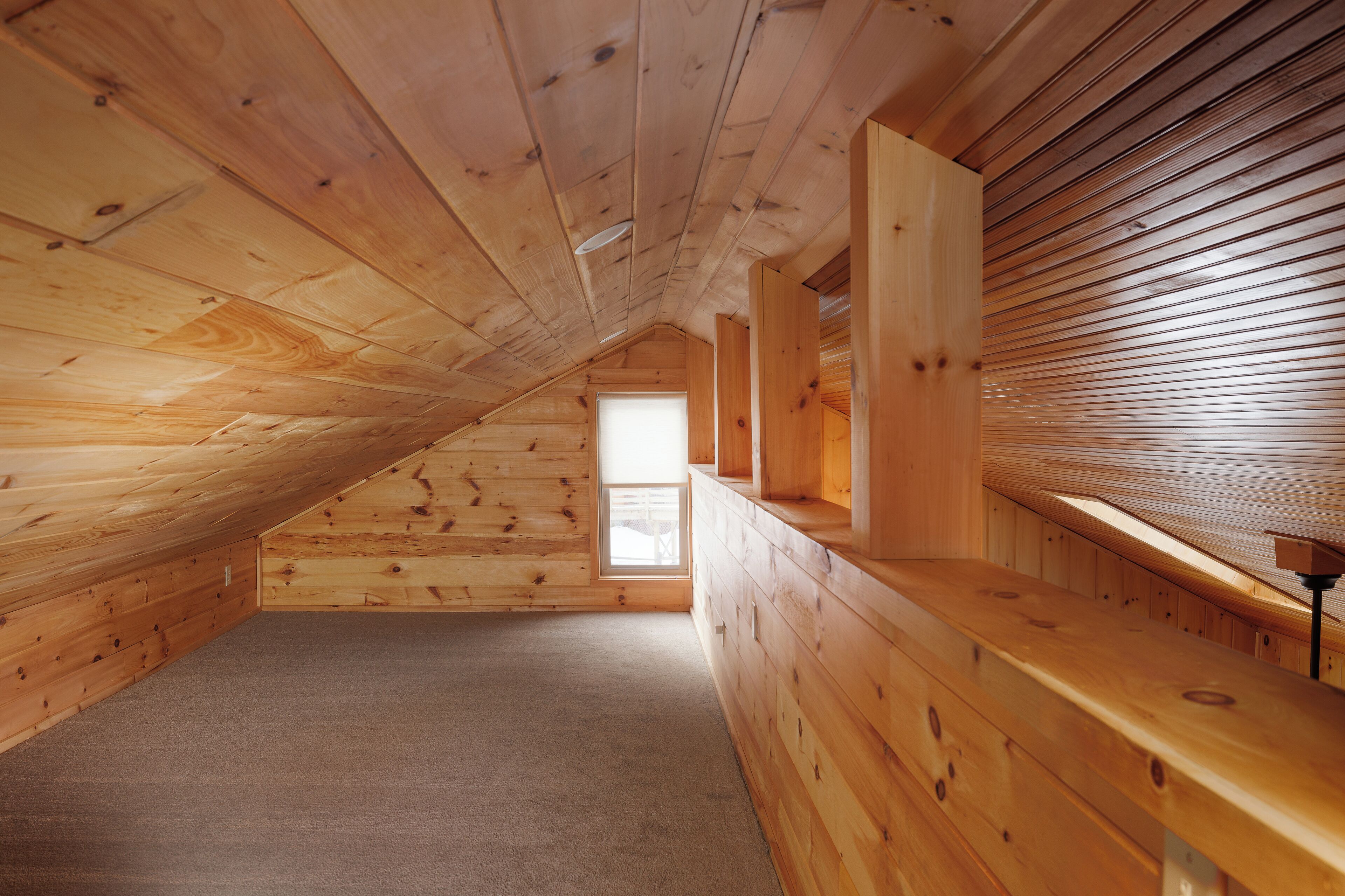Ein Zimmer im Dachgeschoss mit Holzboden, geneigter Decke, einem Fenster und einer fest eingebauten Sitzbank an der Wand.