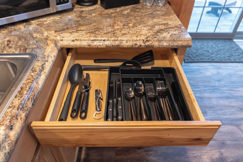 A drawer with kitchen utensils including a spatula, spoon, and knife set.