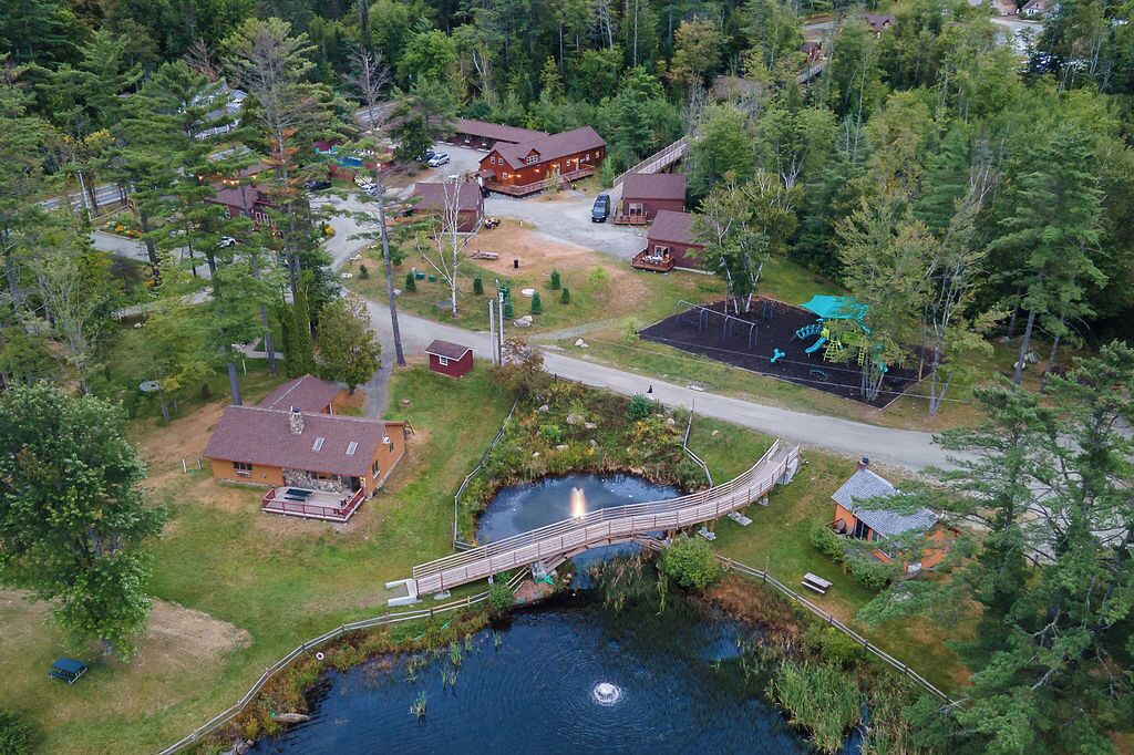 Vista aérea de una propiedad junto al lago con un puente de madera, cabañas y un parque infantil.