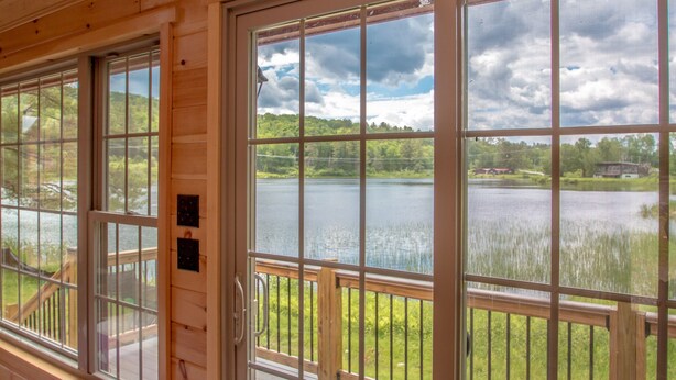 A cabin with large windows overlooking a lake, wooden deck, and a view of the surrounding landscape. - Presidential Mountain Resort (Bethlehem)