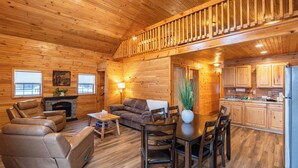 A wooden cabin interior with a dining area, sofas, a fireplace, and a kitchen. - Presidential Mountain Resort (Bethlehem)