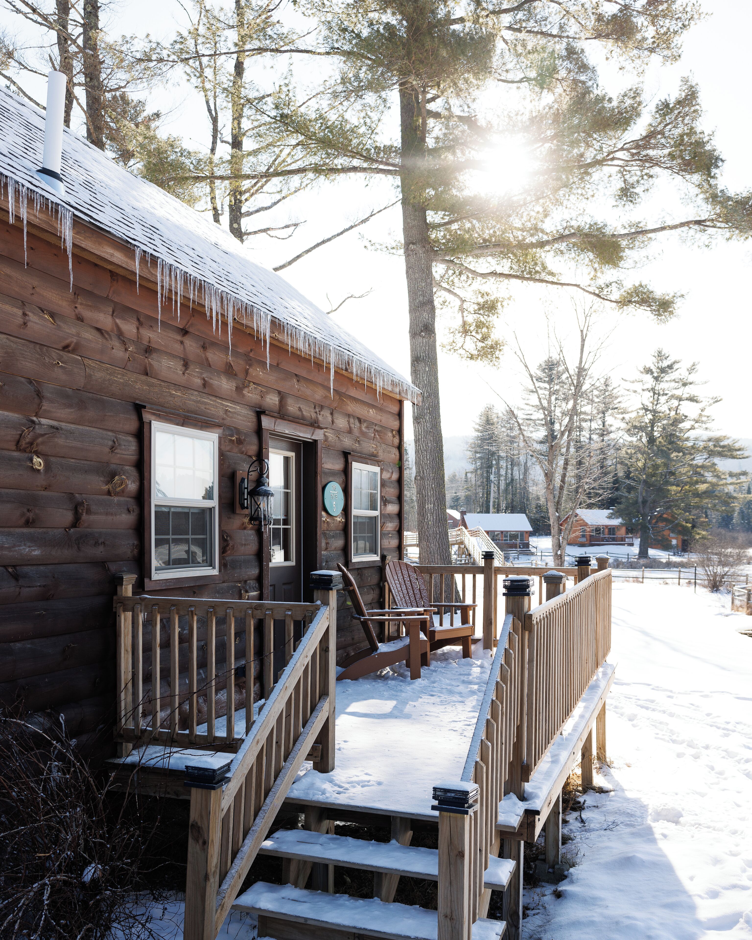 A wooden cabin with a porch, steps, and a snow-covered deck.