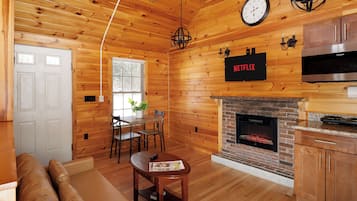 A cozy log cabin interior with a fireplace, wooden walls, a dining area, and a living room with a sofa.