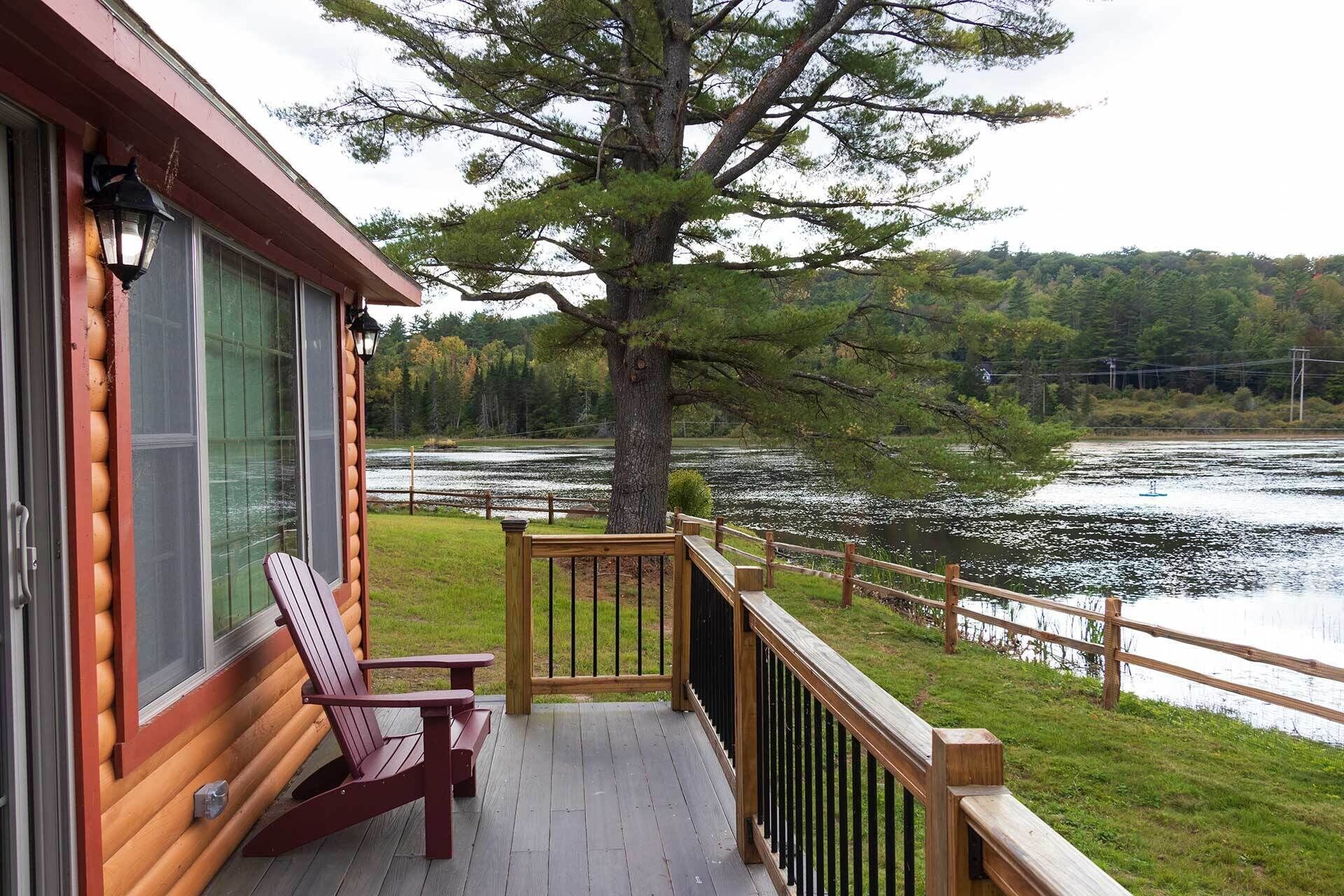 Une terrasse en bois avec une chaise et une table, donnant sur un lac avec un arbre au premier plan.