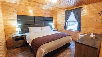 Una habitación con paneles de madera, una cama, mesitas de noche, una ventana con cortinas y un perchero.