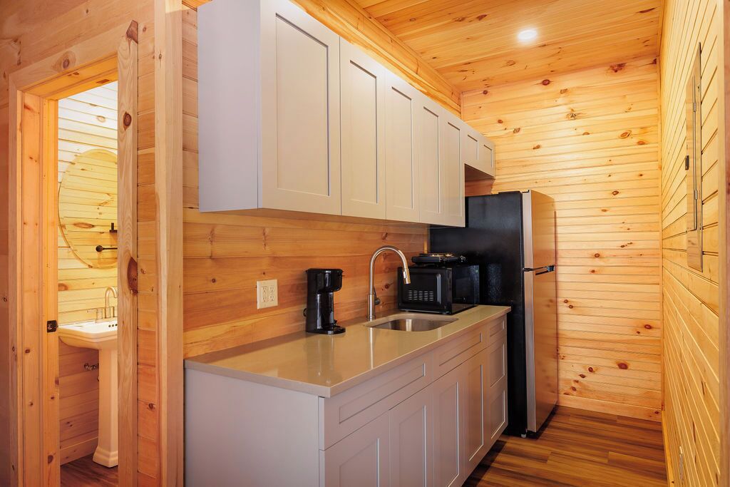 A compact kitchen with wooden walls, a sink, a coffee maker, and a black refrigerator.