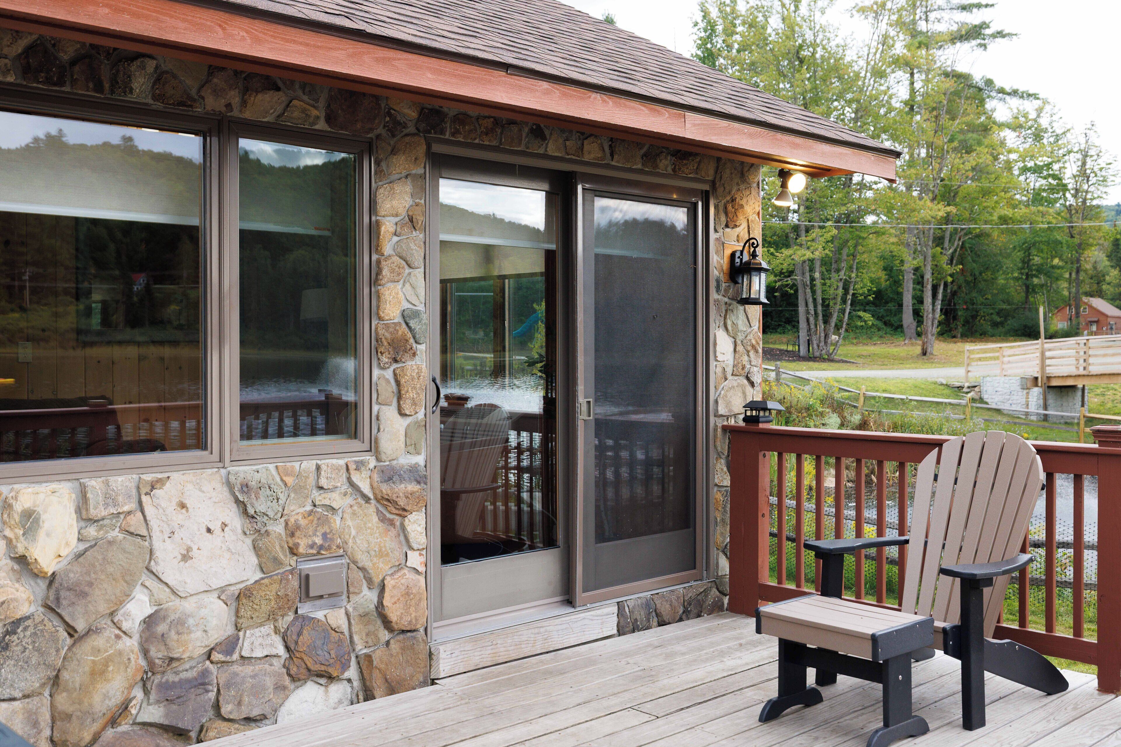 A stone exterior with a wooden deck, a sliding glass door, and a wooden chair.