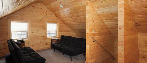 A cozy attic room with wooden walls, a black sofa, a small table, and a window.