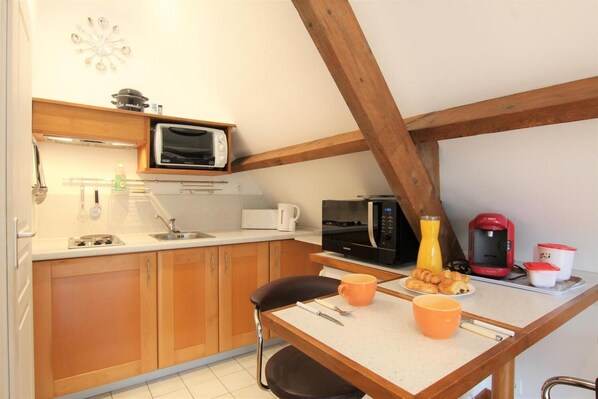 A compact kitchen with wooden cabinets, a microwave, a coffee maker, and a toaster.