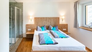 A modern hotel room with a wooden headboard, two beds with matching pillows, a glass shower enclosure, and a window with curtains. - Cozy Holiday Home in Tyrol near Ski Area (Oetz)