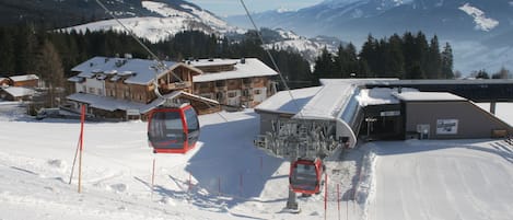 Eine Talstation der Seilbahn mit einer Gondel, Holzbauten und verschneiten Bergen im Hintergrund.