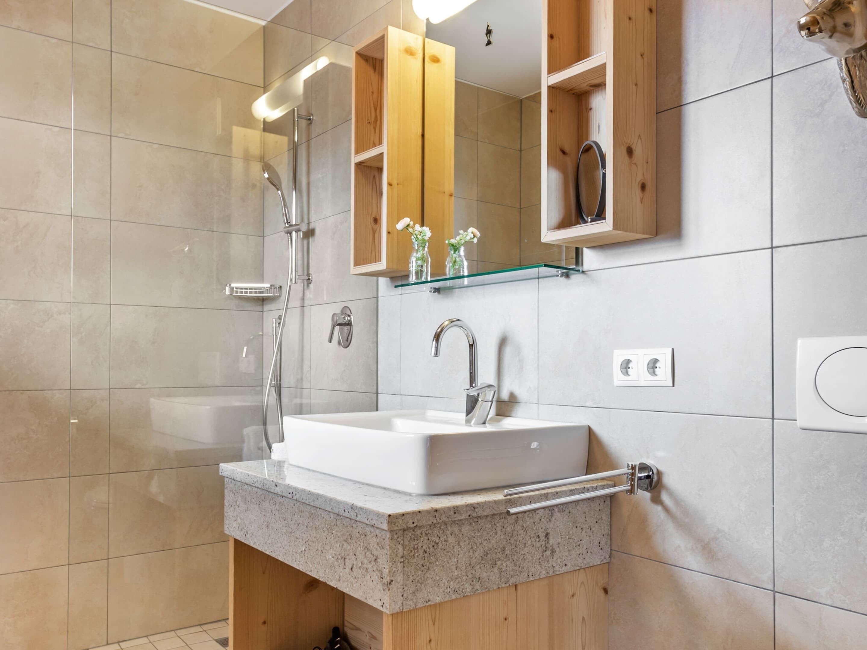 A modern bathroom with a freestanding sink, a glass shelf above the mirror, and a wooden cabinet below.