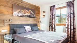 A bedroom with a wooden headboard, a bed with a grey blanket, a bedside table, and a window with curtains. - Unique & Exclusively Furnished Chalet near Ski Lift (Mittersill)