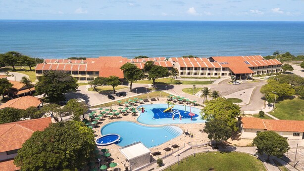 Eine Luftaufnahme eines Resorts mit einem großen Schwimmbad, mehreren Gebäuden mit roten Ziegeldächern und Blick auf den Ozean.