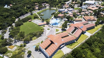 Vista aérea de un complejo turístico con piscina, canchas de tenis y un edificio grande con techo rojo.