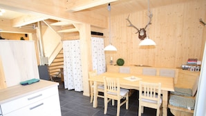 A wooden interior with a dining table, chairs, a bench, a staircase, and a kitchen area. - Lavish Wooded Chalet with Sauna & Hot Tub in Hohentauern (Hohentauern)