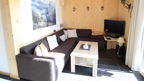 A cozy living room with a sectional sofa, a coffee table, a flat-screen TV, and a mounted painting. - Lavish Wooded Chalet with Sauna & Hot Tub in Hohentauern (Hohentauern)