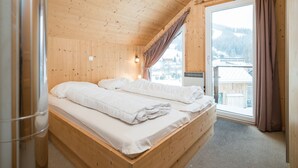 A wooden cabin room with a bed, a window with curtains, and a view of a snowy landscape. - Chalet in Hohentauern Near Ski Lift (Hohentauern)
