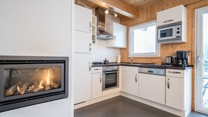 A modern kitchen with a built-in fireplace, stainless steel appliances, and wooden ceiling beams. - Chalet in Hohentauern Near Ski Lift (Hohentauern)