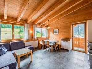 A cozy wooden cabin interior with a dining area, sofa, and large windows offering a view of the outdoors.