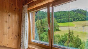 A wooden cabin with a large window offering a view of a forested area and a field. - Cozy Apartment in Fendels near Ski Area (Fendels)