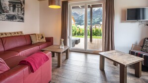 A cozy living room with a red leather sofa, wooden tables, and a large window with a view of mountains. - Spacious Chalet in Kötschach-Mauthen near Ski Area (Kotschach-Mauthen)