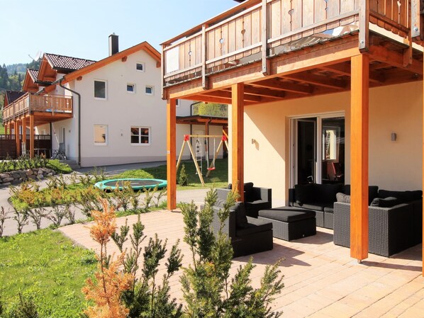 A covered outdoor area with a swing set, a trampoline, and outdoor seating.