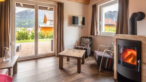 A cozy living room with a fireplace, a television, and a view of a mountain landscape. - Spacious Chalet in Kötschach-Mauthen near Ski Area (Kotschach-Mauthen)