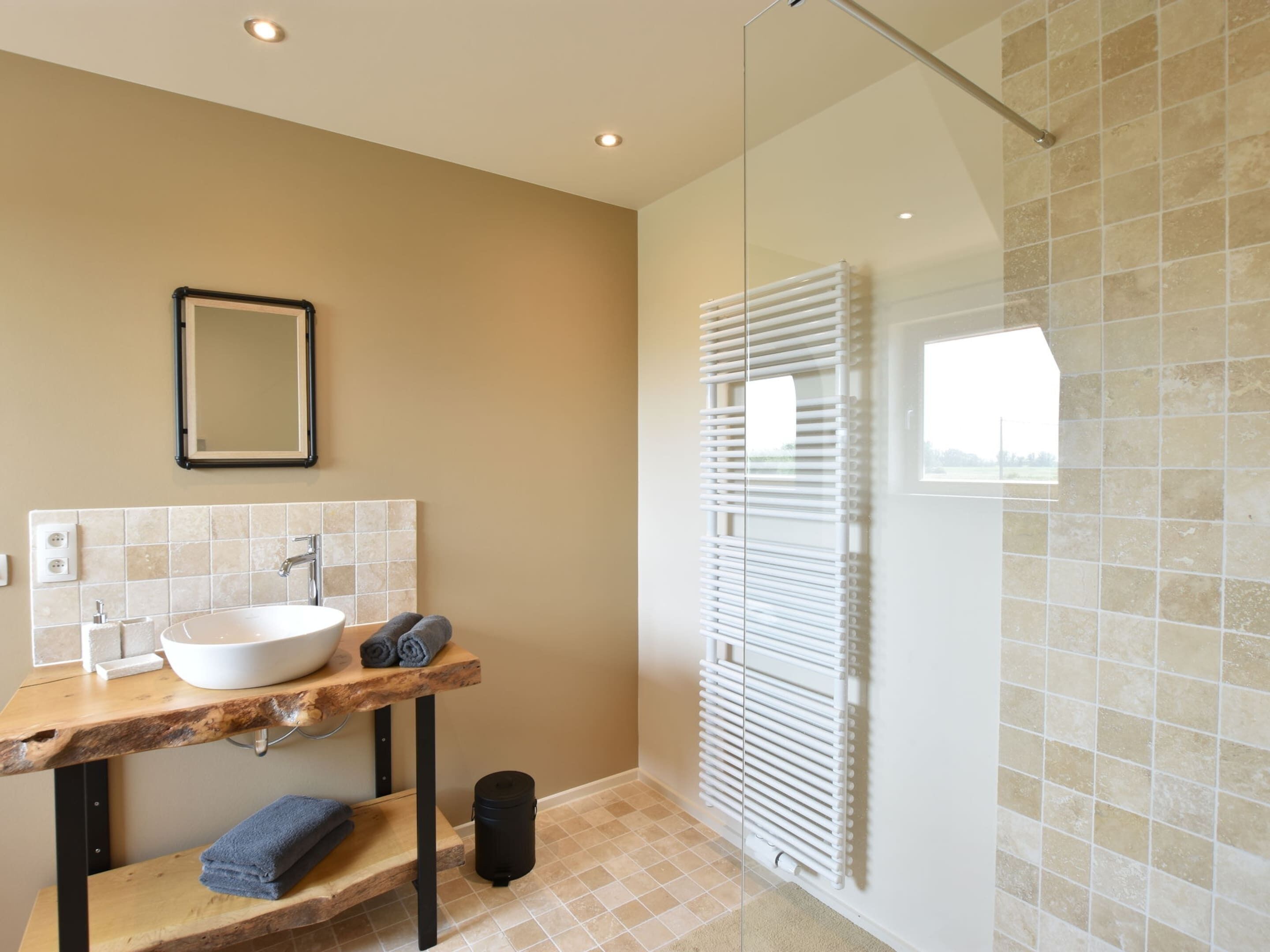 Une salle de bain moderne avec un meuble-lavabo en bois, un lavabo blanc, un miroir et une cabine de douche en verre.