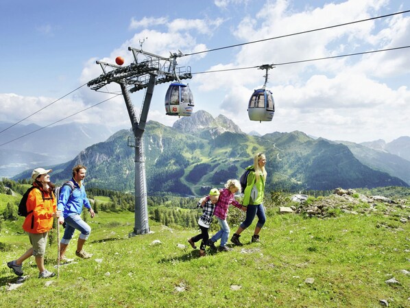 A group of people walking on a mountain path with a cable car system in the background.