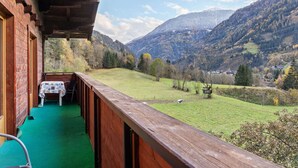 Ein Holzbalkon mit Tisch und Stühlen, mit Blick auf ein grünes Feld und Berge.