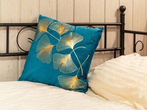 A bed with a teal pillow featuring a leaf pattern and a white comforter.