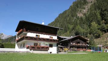 Eine zweistöckige Chalet mit Balkonen, umgeben von einer üppigen grünen Wiese und einer gebirgigen Kulisse.