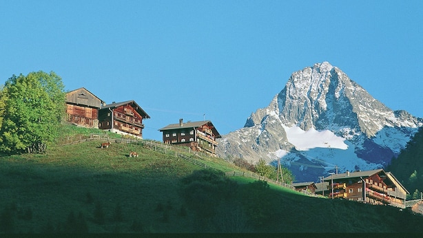 Ein Chalet in den Bergen mit steilem Dach, Holzfassade und einem Balkon.