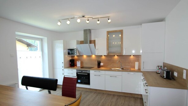 A modern kitchen with white cabinets, a wooden countertop, and a dining area with a wooden table and chairs. - Country House in Koetschach-mauthen in ski Area (Kotschach-Mauthen)