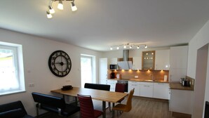 A modern kitchen with white cabinets, a microwave, and a stove. There is a dining area with a wooden table and chairs. - Country House in Koetschach-mauthen in ski Area (Kotschach-Mauthen)