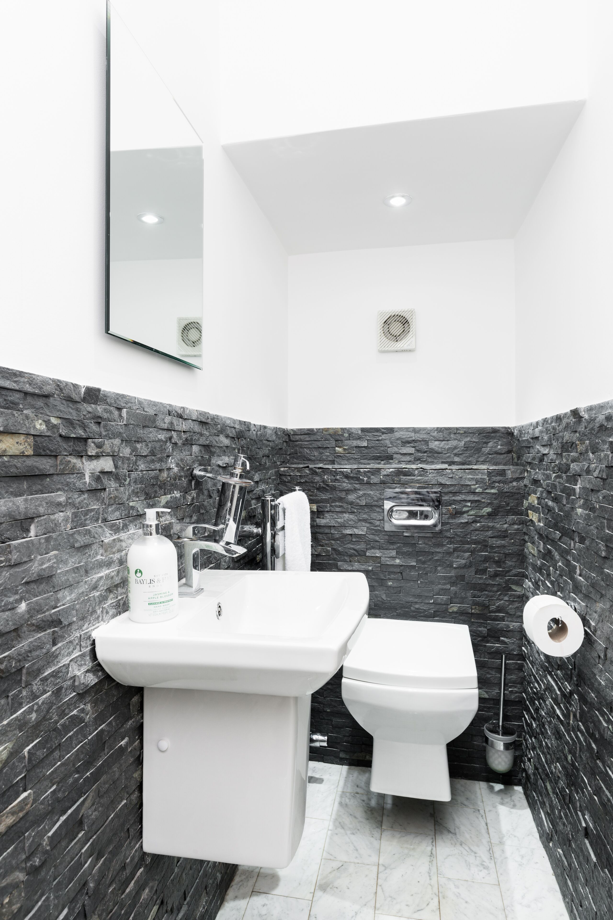 A bathroom with a stone wall, a sink, a toilet, and a mirror.