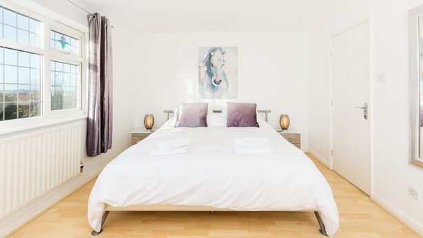 A bedroom with a large bed, a painting of a horse on the wall, and a window with curtains.
