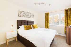 A bedroom with a bed, a nightstand, a lamp, a window with curtains, and a radiator.