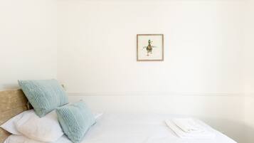 A neatly made bed with white linens and a folded towel, a pillow, and a framed picture on the wall.